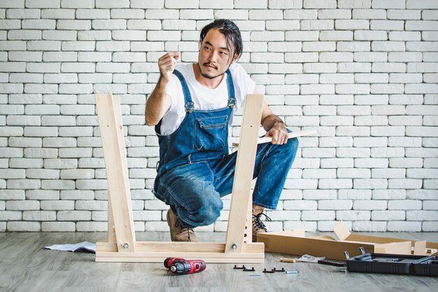 Hombre joven inconformista trabajando como manitas, montaje de mesa de madera con equipos,