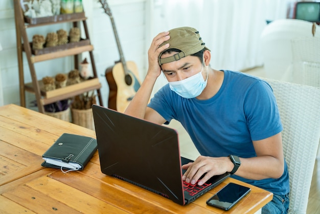 Hombre joven independiente con mascarilla que trabaja con la computadora portátil y se siente triste