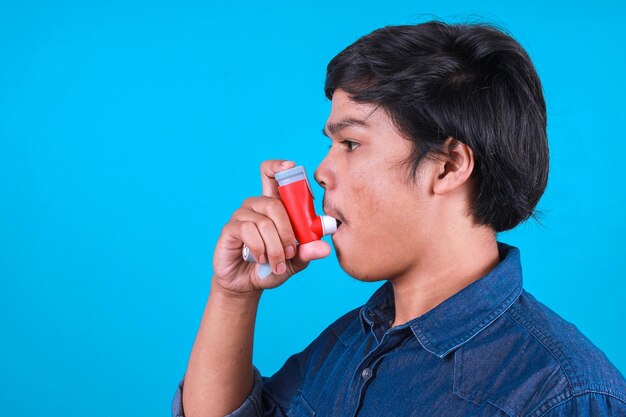 Hombre joven con inhalador con ataque de asma en fondo azul