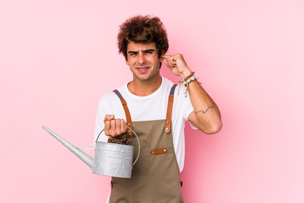 Hombre joven jardinero caucásico aislado cubriendo las orejas con las manos.