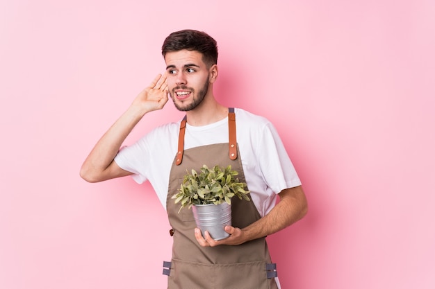 Hombre joven jardinero caucásico sosteniendo una planta aislada tratando de escuchar un chisme.