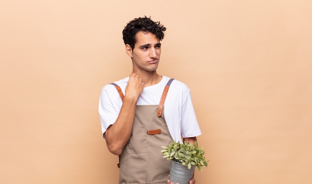 Hombre joven jardinero que se siente estresado, ansioso, cansado y frustrado, tirando del cuello de la camisa, luciendo frustrado con el problema