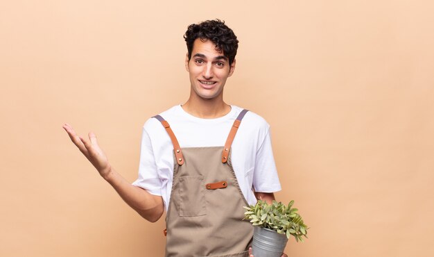 Hombre joven jardinero que se siente feliz, sorprendido y alegre, sonriendo con actitud positiva, dándose cuenta de una solución o idea