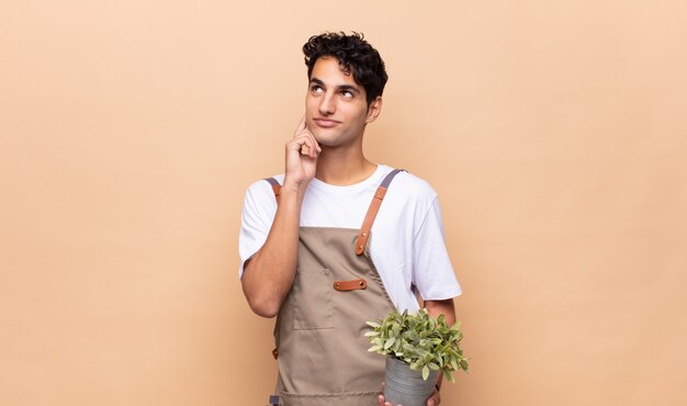 Hombre joven jardinero sonriendo felizmente y soñando despierto o dudando, mirando hacia un lado