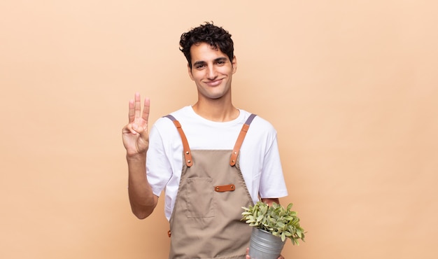 Hombre joven jardinero sonriendo y mirando amigable, mostrando el número uno o el primero con la mano hacia adelante, contando hacia atrás
