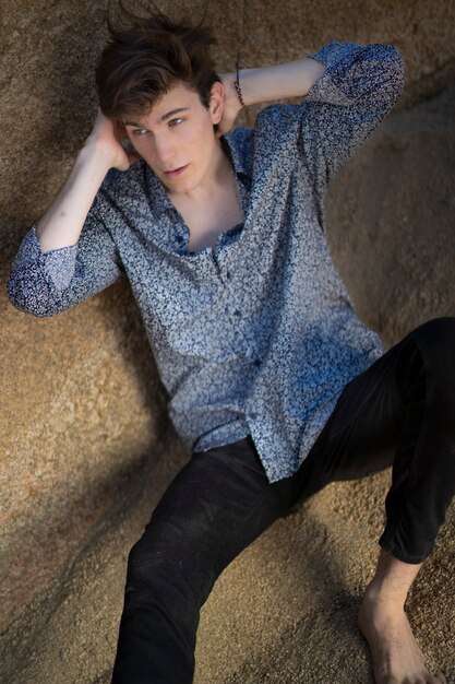 Hombre joven con jeans y camisa blanca entre rocas