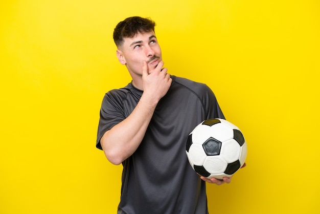 Hombre joven jugador de fútbol aislado sobre fondo amarillo que tiene dudas