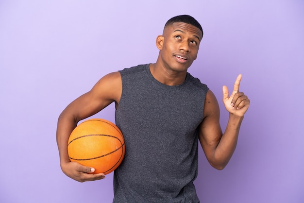 Hombre joven jugador latino de baloncesto aislado en la pared púrpura pensando en una idea apuntando con el dedo hacia arriba