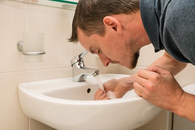 Hombre joven lavándose la cara. Cuarto de baño.