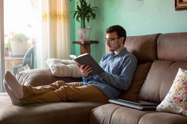 Hombre joven con el libro en el sofá en casa