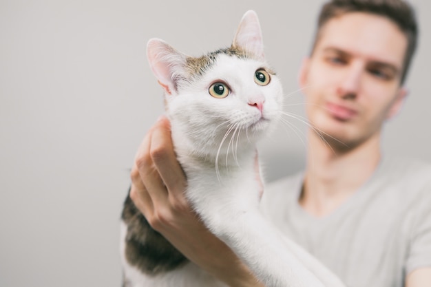 Hombre joven con lindo gato gracioso sobre fondo claro