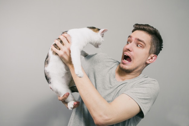 Hombre joven con lindo gato gracioso sobre fondo claro