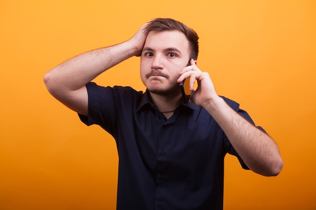 Hombre joven con la mano en la cabeza mientras habla por teléfono. Joven irritado