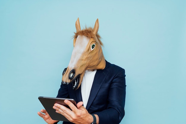 Hombre joven con máscara de caballo divertido trabaja con una tableta portátil.