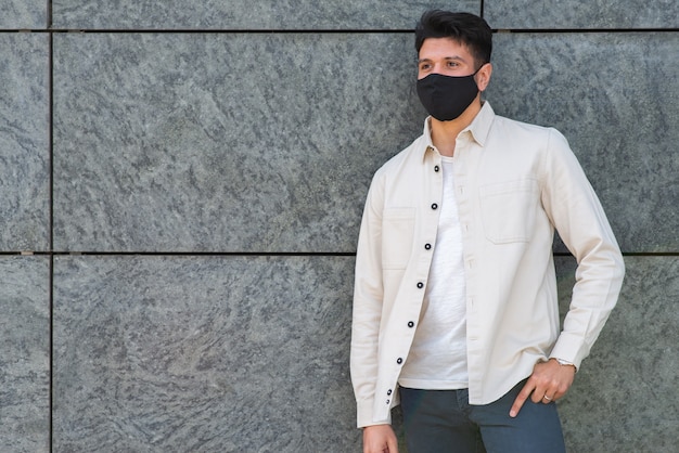 Hombre joven con máscara de covid o coronavirus apoyado contra una pared en una ciudad