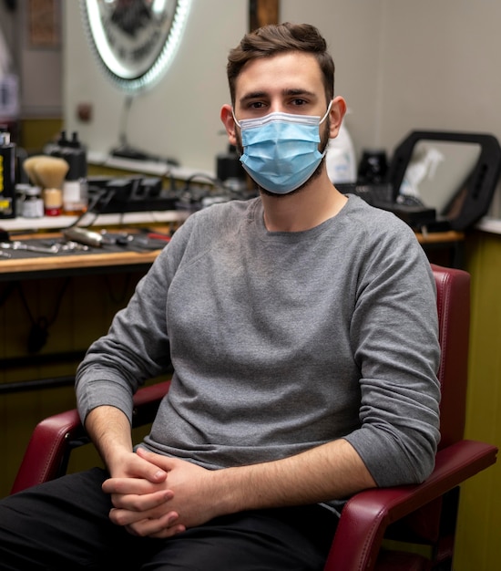 Hombre joven con máscara médica esperando en la peluquería