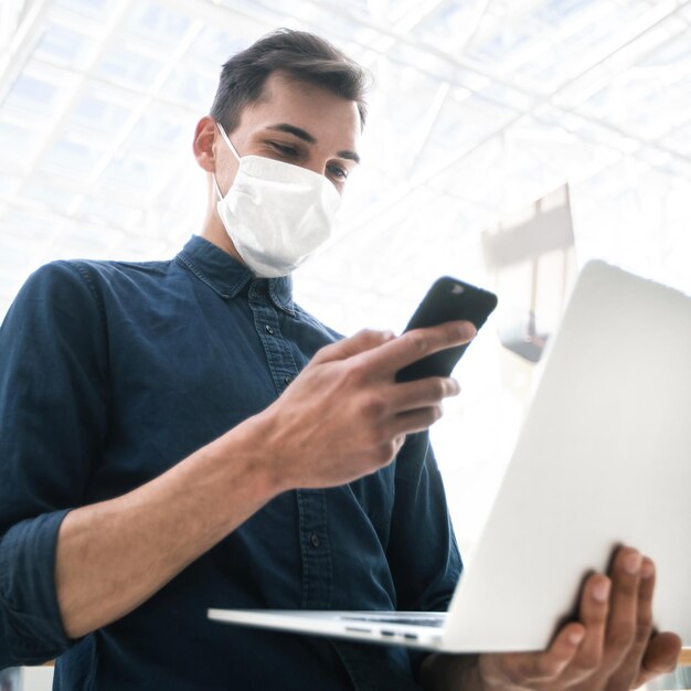 El hombre joven con una máscara protectora está eligiendo un contacto en su teléfono inteligente. pandemia en la ciudad