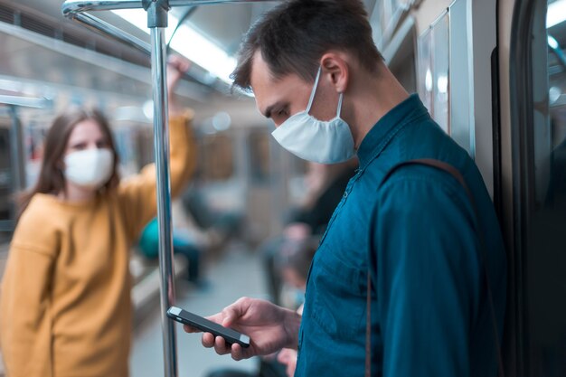 Hombre joven con una máscara protectora mirando la pantalla de su teléfono inteligente. coronavirus en la ciudad