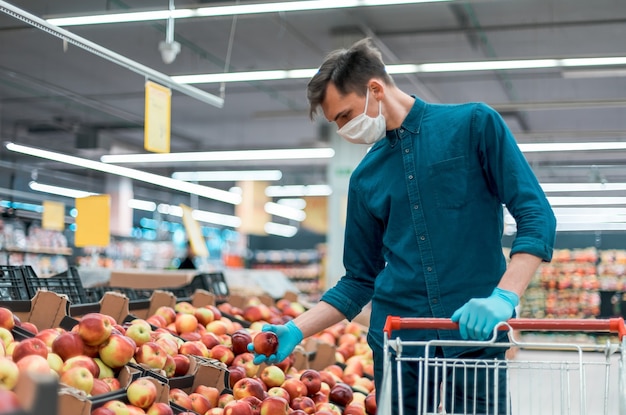 Hombre joven con una máscara protectora de pie cerca del mostrador con manzanas. foto con copia del espacio