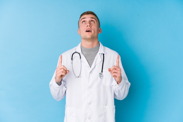 Hombre joven médico caucásico apuntando al revés con la boca abierta.