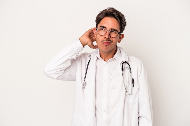 Hombre joven médico de raza mixta aislado sobre fondo blanco tocando la parte posterior de la cabeza, pensando y haciendo una elección.