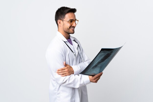 Hombre joven médico sosteniendo una radiografía aislada en blanco mirando hacia el lado