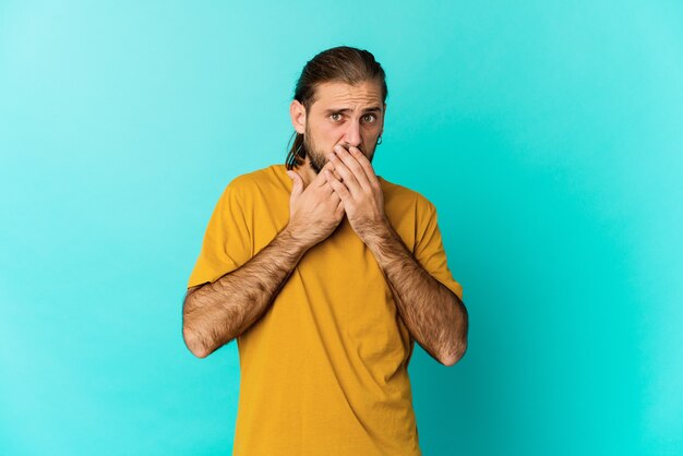 Hombre joven con mirada de pelo largo cubriendo la boca con las manos mirando preocupado.