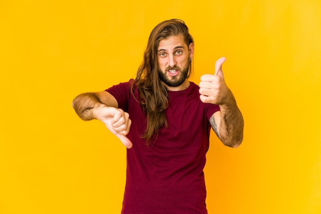 Hombre joven con mirada de pelo largo mostrando los pulgares hacia arriba y hacia abajo, concepto de elección difícil