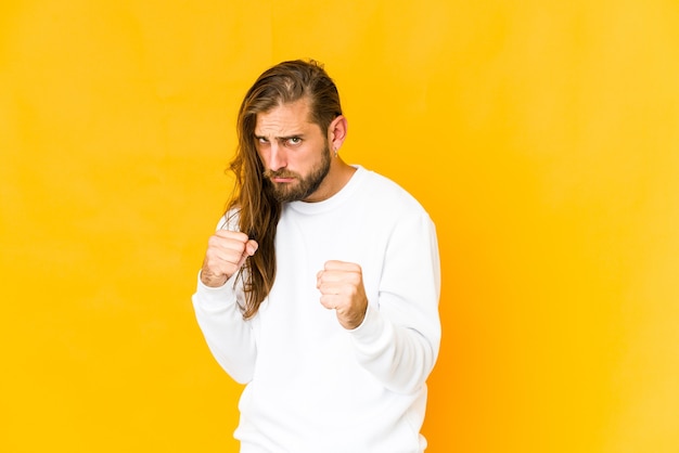 Hombre joven con mirada de pelo largo mostrando puño, expresión facial agresiva.