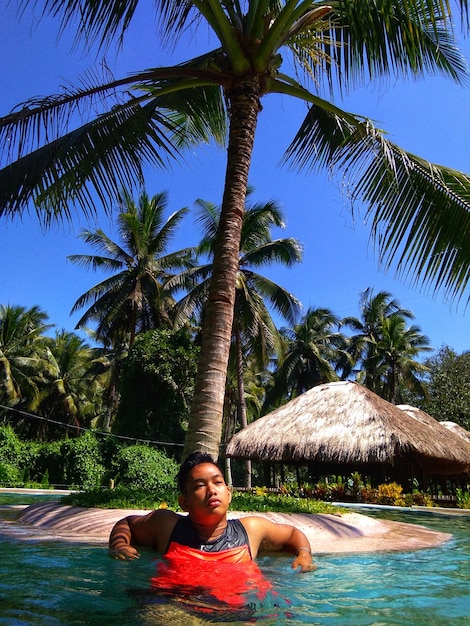 Foto hombre joven mirando hacia otro lado mientras se relaja en la piscina contra el cielo