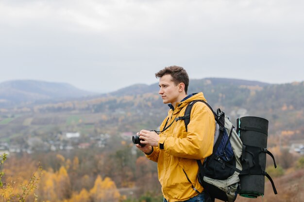 Hombre joven con mochila toma una foto con una cámara de cine en las montañas