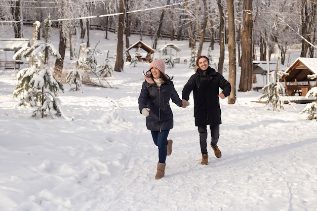 Hombre joven y mujer corriendo en un parque de invierno cubierto de nieve