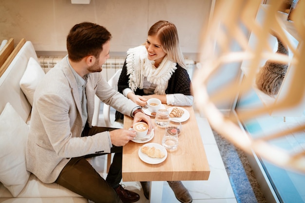 Hombre joven y mujer joven sentados en el café y hablando con una sonrisa. Ellos bebiendo café y desayunando. Vista superior.