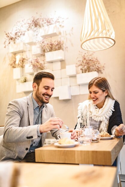 Hombre joven y mujer joven sentados en el café y hablando con una sonrisa. Ellos bebiendo café y desayunando.