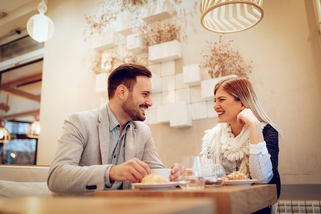 Hombre joven y mujer joven sentados en el café y hablando con una sonrisa. Ellos bebiendo café y desayunando.