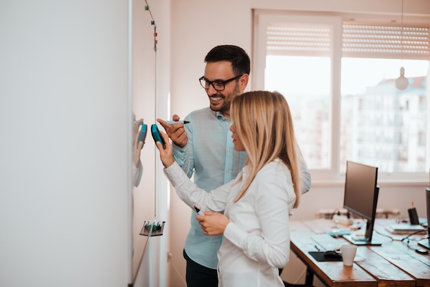 Hombre joven y mujer que hacen notas en un whiteboard en oficina.