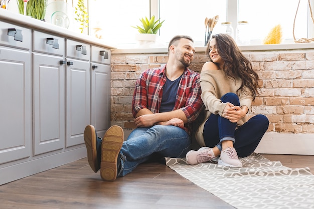 Hombre joven y mujer sentada en el piso de la cocina y hablando. Amante joven pareja pasar tiempo juntos en casa.