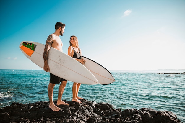 Foto hombre joven y mujer con tablas de surf en roca cerca del mar