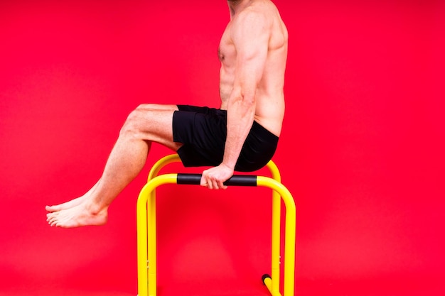 Hombre joven musculoso haciendo ejercicios de barra paralela en un estudio rojo blanco oscuro con espacio de copia