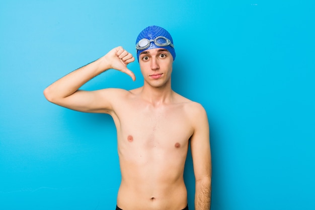 Hombre joven nadador mostrando un gesto de disgusto, pulgares abajo. Concepto de desacuerdo