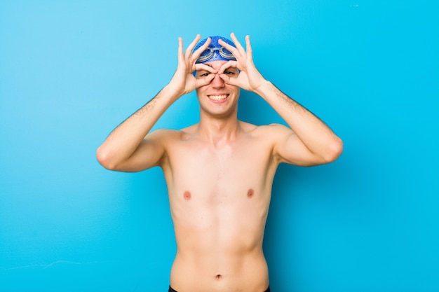 Hombre joven nadador mostrando signo bien sobre los ojos