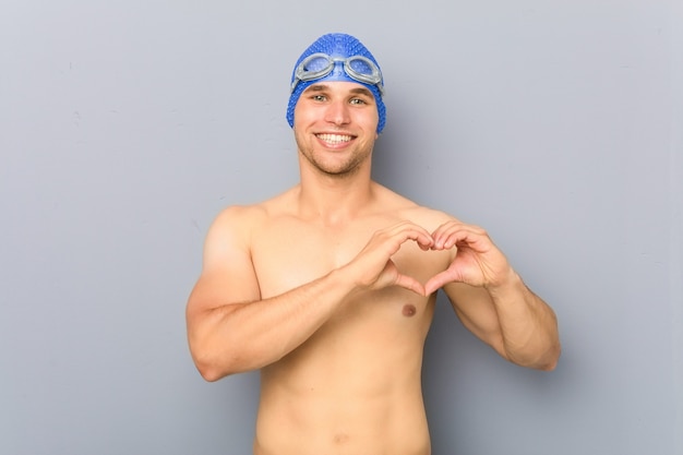 Hombre joven nadador profesional sonriendo y mostrando una forma de corazón con las manos.