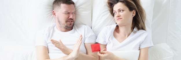 Hombre joven se niega a usar condones mientras está acostado con la mujer en la cama métodos anticonceptivos masculinos
