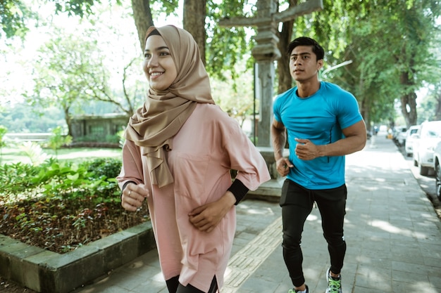 Un hombre joven y una niña con un pañuelo en la cabeza haciendo jogging juntos cuando hacen ejercicio al aire libre en el parque