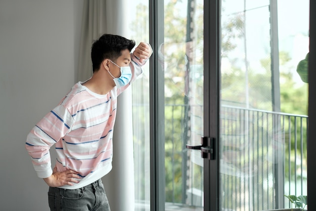 Hombre joven durante la pandemia de coronavirus con mascarilla en el interior de su casa por distanciamiento social