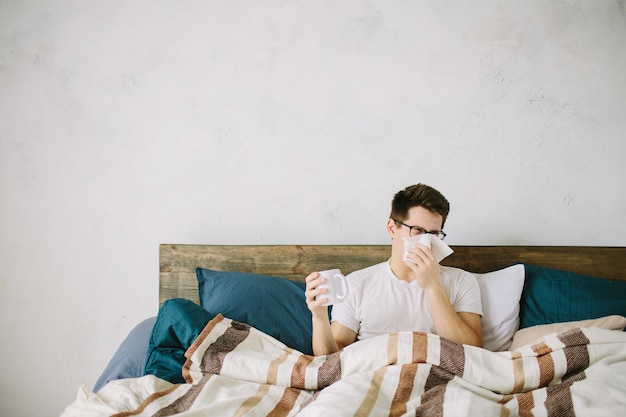 Hombre joven con pañuelo. El enfermo en la cama tiene secreción nasal. el hombre hace una cura para el resfriado común.