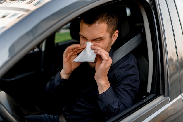 Hombre joven con pañuelo. El enfermo tiene goteo nasal. El modelo masculino cura el resfriado común en el automóvil.