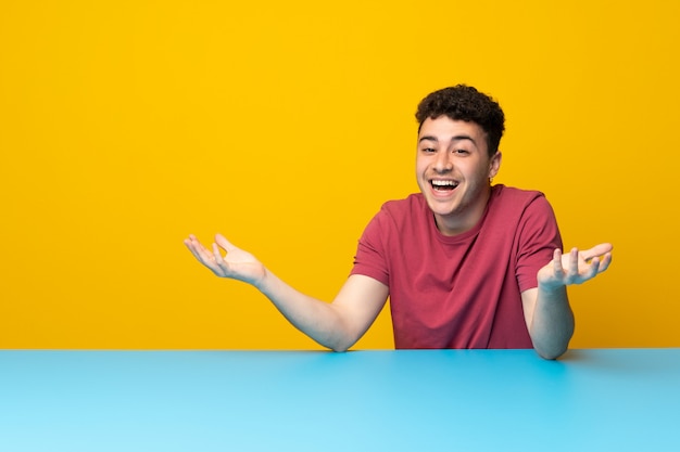 Hombre joven con pared de colores y mesa sonriendo mucho