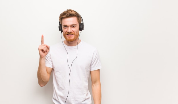 Hombre joven pelirrojo mostrando el número uno. Escuchar música con auriculares.