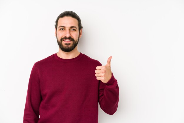 Hombre joven de pelo largo en una pared blanca sonriendo y levantando el pulgar